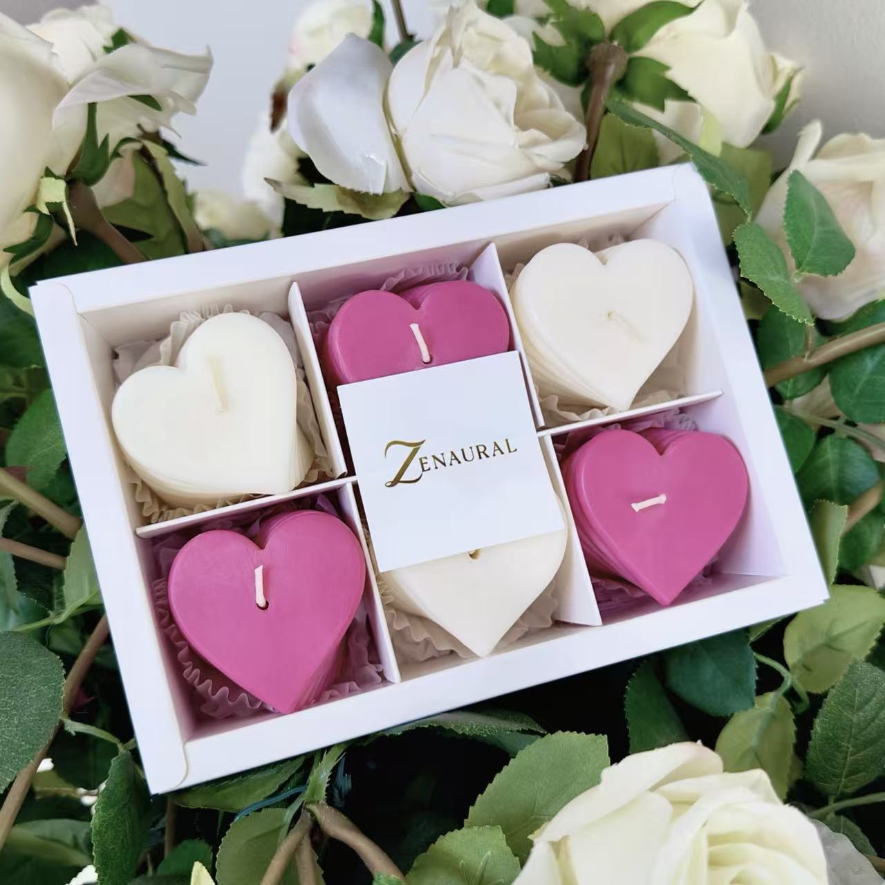 Heart-shaped spiral candles in deep pink and white, presented in a Zenaural box surrounded by fresh white roses.