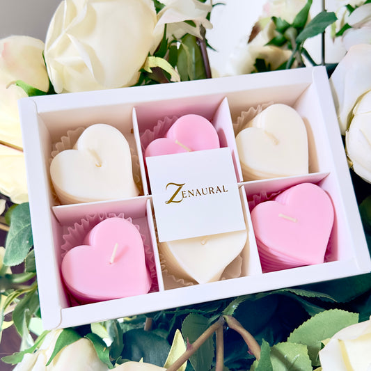 Heart-shaped spiral candles in blush pink and white, arranged in a Zenaural gift box among white roses.