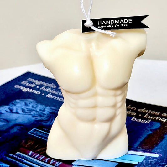 “Handmade sculpted male torso candle in ivory white, featuring detailed muscle contours, decorative hang tag, and artistic display background.”