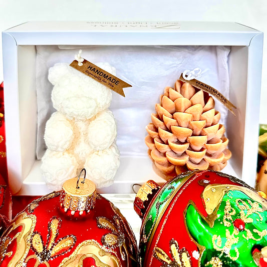 White bear and brown pinecone sculptural candles in a white gift box, with festive red-green ornaments
