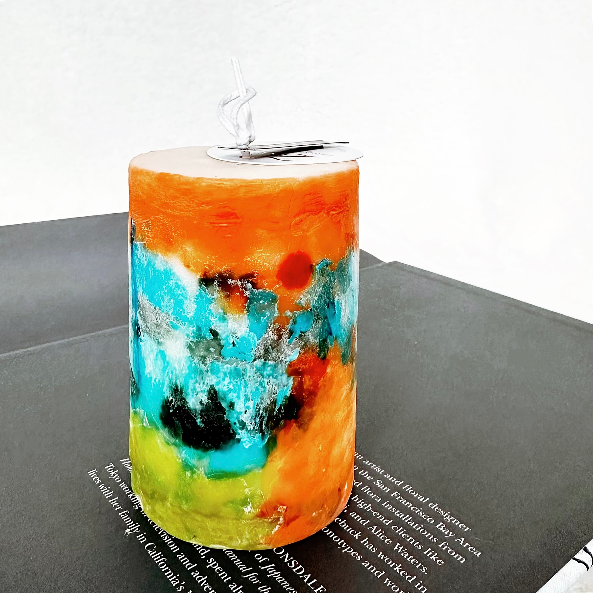 Poème en Cire — Impression de Lumière hand-painted art pillar candle with swirls of sunrise orange, azure blue, and moss green, Zenaura Studio.